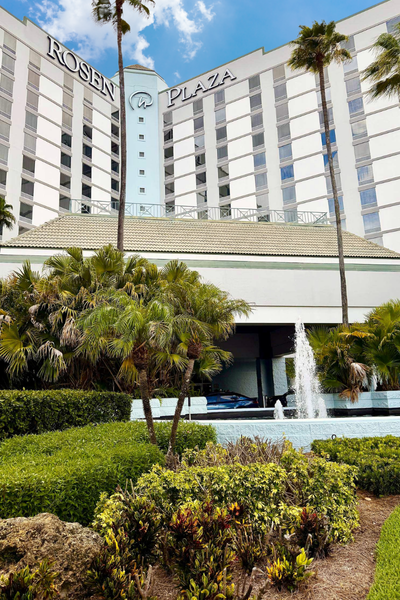 The front entrance of Rosen Plaza with a fountain, landscaped gardens, and tall palm trees.