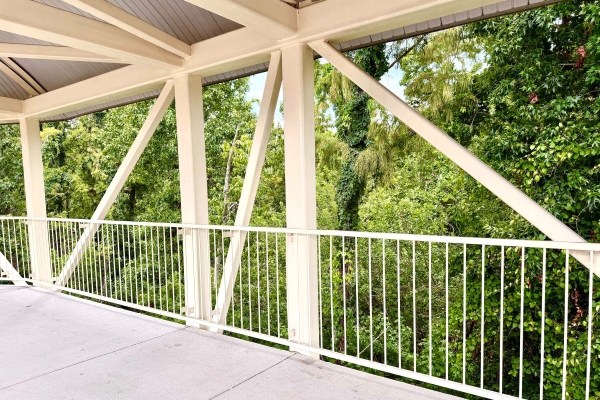White structure beams and a railing create an angular barricade against a backdrop of lush trees.