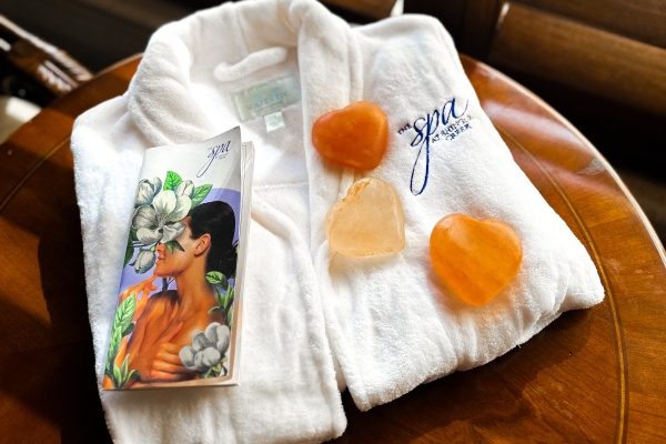A folded white spa robe with the Spa at Shingle Creek logo, with a spa brochure and salt stones resting on top.