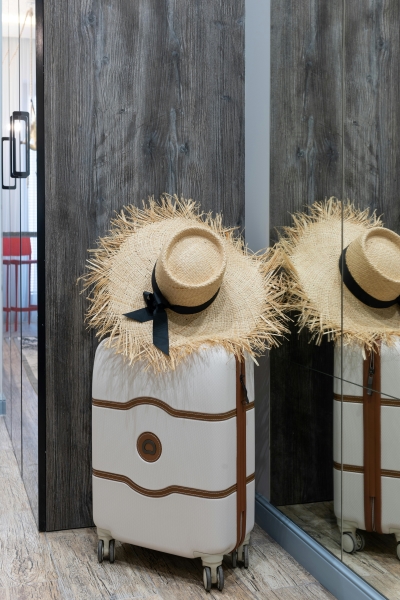 A white suitcase with brown accents and trim and a straw hat with a black ribbon resting on top.  