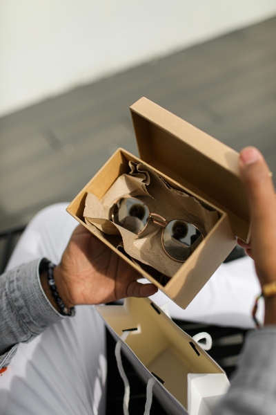 A man’s hands opening a brown box with a pair of stylish sunglasses inside.  