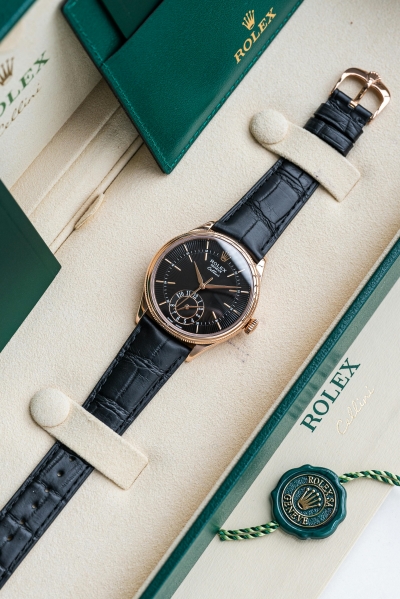 A green box with an ivory lining and a gold Rolex label with a black watch with a black leather band.