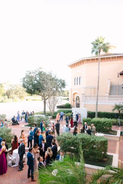 An outdoor courtyard with landscaped hedges and trees filled with a group of wedding guests. 
