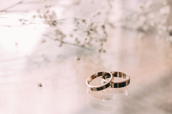 Two gold wedding rings stacked on a shiny marble surface in front of out-of-focus sprigs of baby's breath.