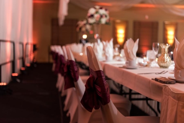 A close-up of white linen-covered chairs tied with maroon sashes seated at a long table at a formal event.