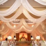 A glowing ballroom space with swaths of white linen hanging from the ceiling over tables and a dance floor.