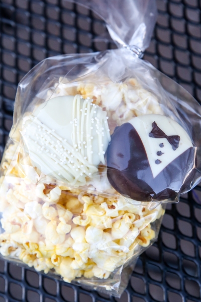 A bag of popcorn and two dipped oreos designed to look like a bride and groom. in a cellophane baggie.