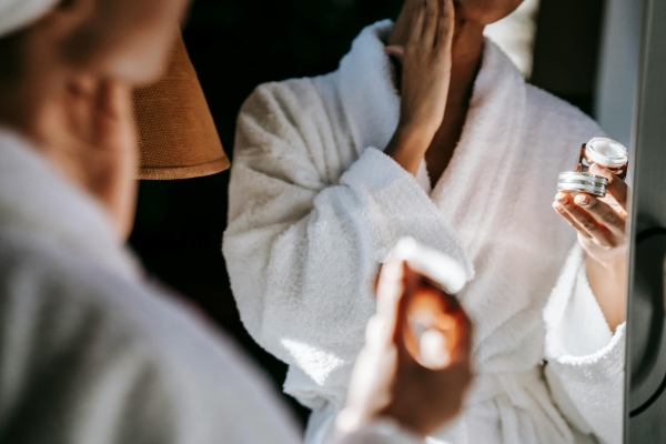 A closeup of a woman in a white robe holding a jar of face cream.  