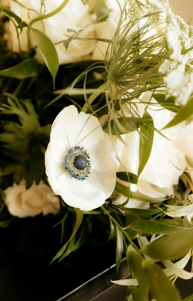 A close-up of a winter wedding bouquet with lots of greenery and a pristine white ranunculus flower. 
