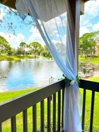 A panel of sheer fabric tied to a gazebo post overlooking a pond, grass, and trees. Rosen Inn Lake Buena Vista has a beautiful outdoor pavilion for a hotel wedding.