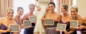 Bridesmains hold chalkboard signs with the words "Wait Until You See Her" in front of bride