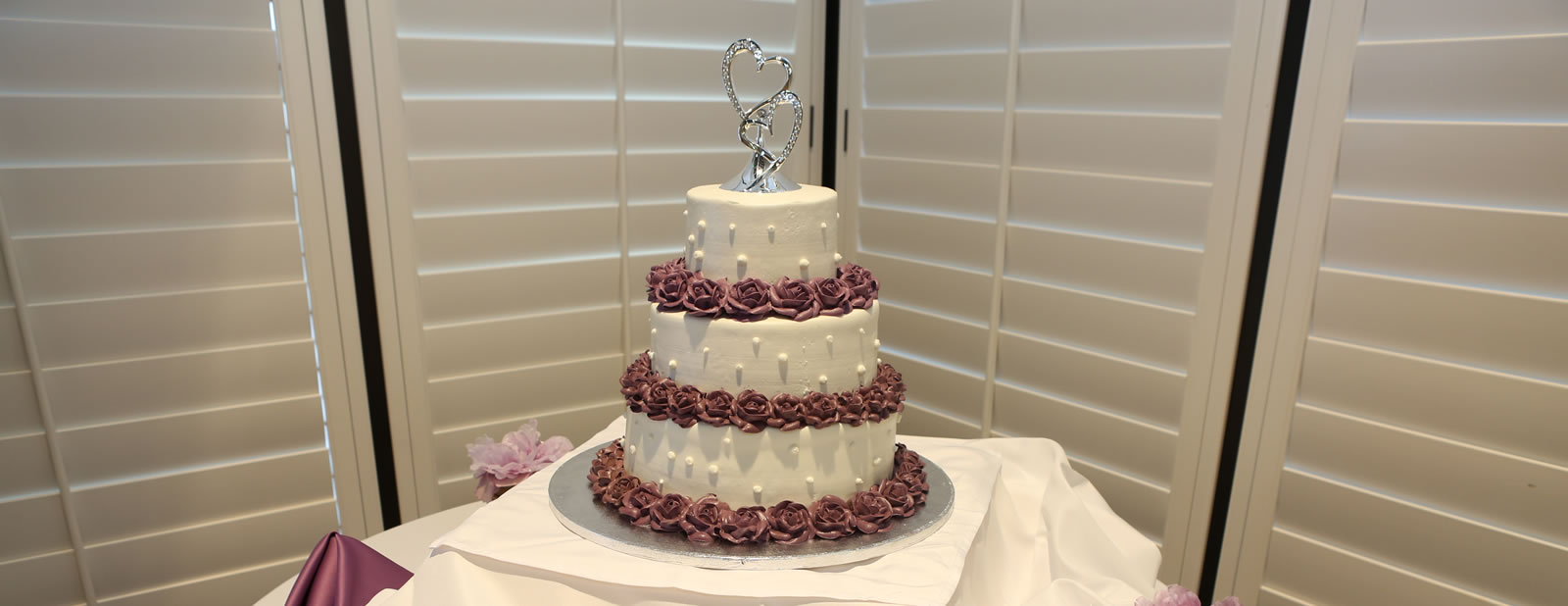 White 3 tier cake with purple roses and silver hearts on top