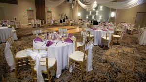 Weddings table setup with white table cloths, purple napkinds, and gold and white chairs