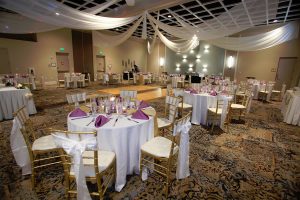 Clarion table set up for wedding reception with white and gold chairs, white tablecloth, and purple napkins