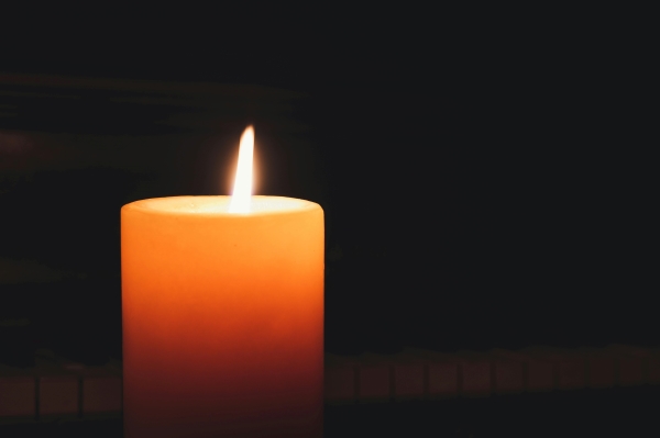 A lit pillar candle glowing orange against a black backdrop.