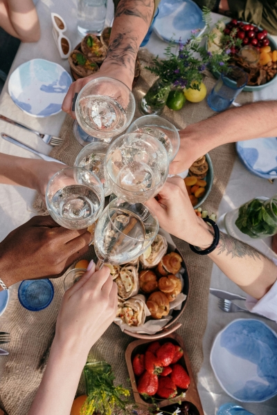 An aerial view of six hands toasting glasses of Champagne over a table of fresh fruit, wildflowers, and rustic table settings. 