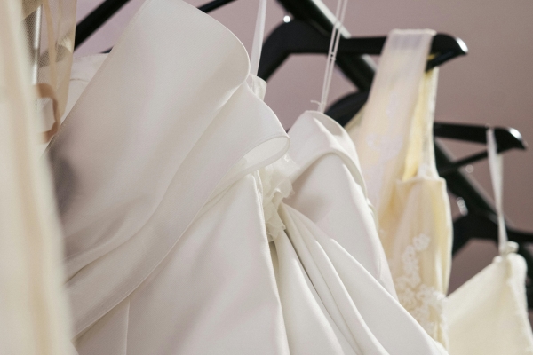 A close-up of a row of wedding gowns hanging on dark hangers.