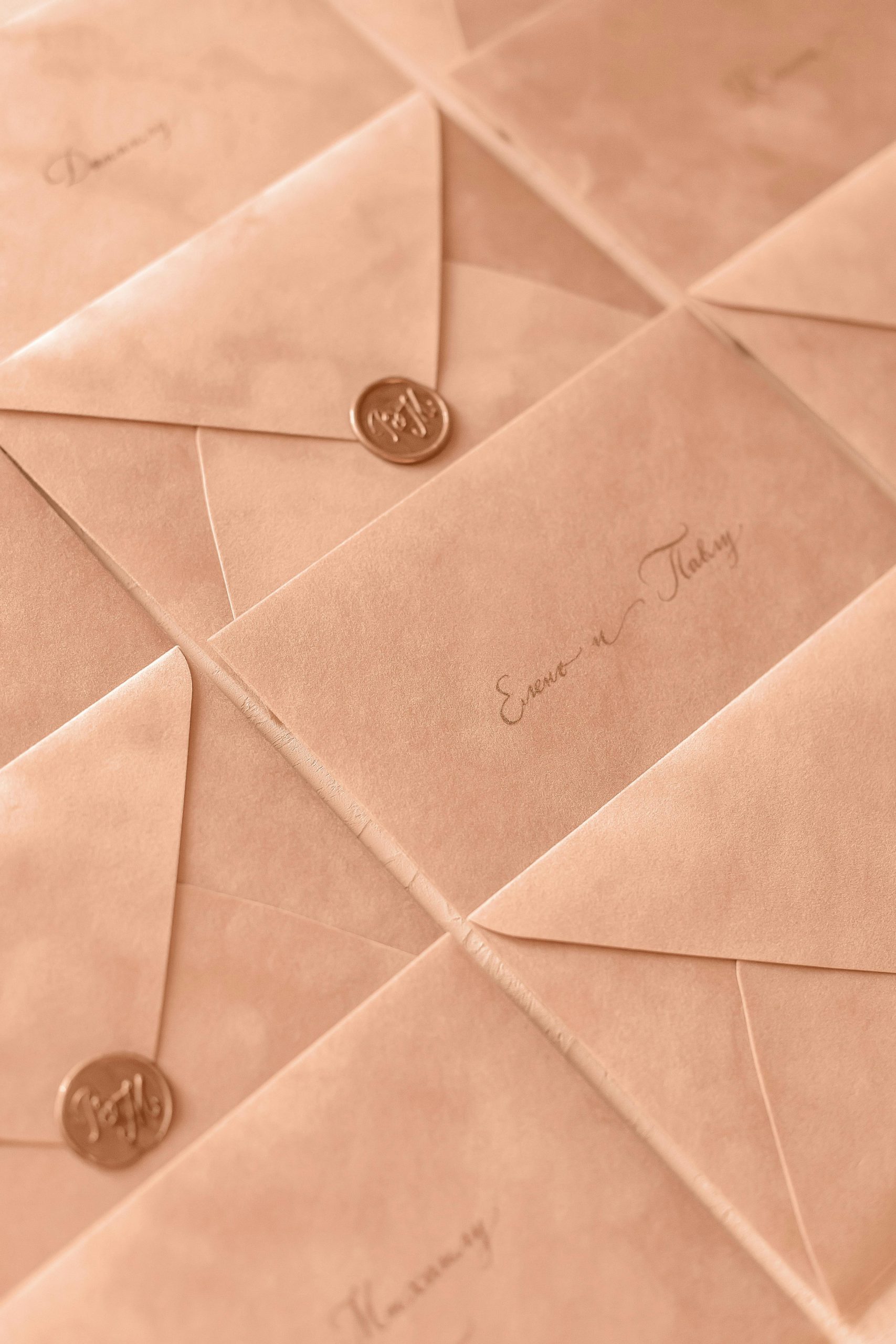 Many save-the-date envelopes next to each other with gold wax seals and names written on them in an elegant font. 