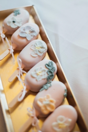 A row of pale pink cake pops decorated with leaves and flowers presented on a gold tray. Cake pops are an elegant single-serving dessert alternative that offer the perfect pop of sweetness. 