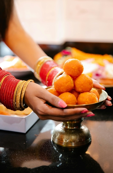 Hands with pink fingernails and dozens of red and gold bangles sets a dish of round pastries on a table 