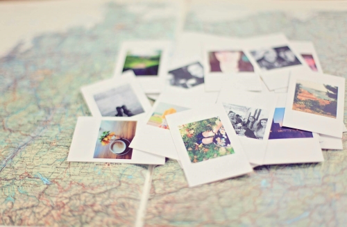 A pile of polaroid photos on top of a map. A unique bridesmaid proposal idea is sharing photos and memories that emphasize the importance of your relationship.