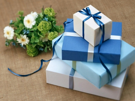 Four boxes wrapped in blue and white ribbons and wrapping paper beside a green and white bouquet. Many guests prefer to give gifts purchased from a wedding registry.