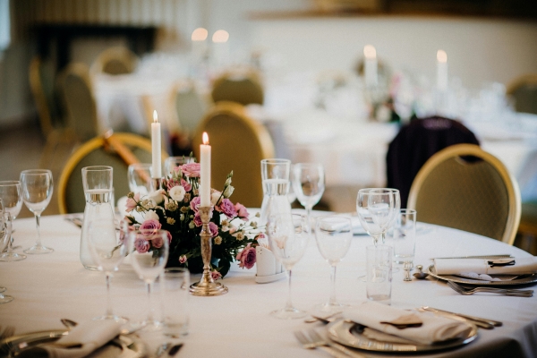 A formally set round table with a centerpiece of tall candles and pink and white flowers. 