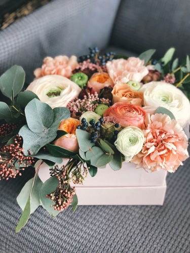 A bouquet of peach, pink, and white flowers with greenery in a pale pink box. Sending a beautiful floral arrangement is a great bridesmaid proposal idea.