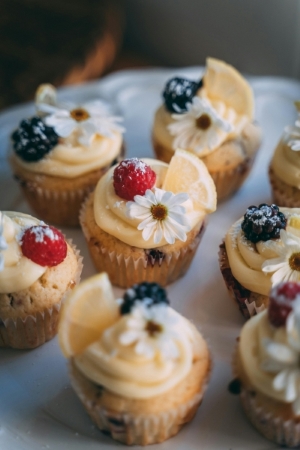 A plate of vanilla cupcakes decorated with daisies, berries, and lemon slices. Cupcakes are a wedding dessert alternative for couples who want the taste of cake without the cost.