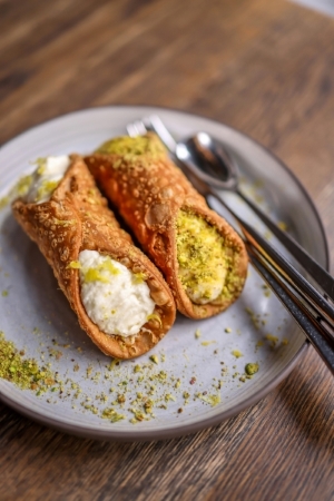 Two small cannoli on a plate dusted with green pistachios. Classic Cannoli make a fabulous wedding dessert alternative.