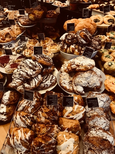 A display of dozens of different kinds of pastries, some dusted with powdered sugar, others drizzled in chocolate and icing. 