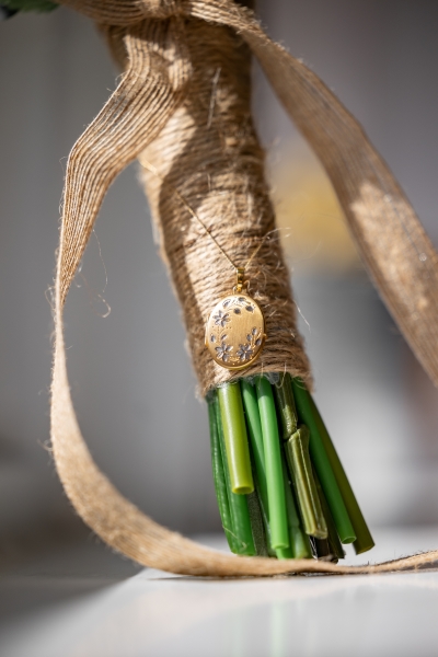  A close-up on green stems of a bouquet wrapped in brown twine with a gold and silver floral locket tied around it. 