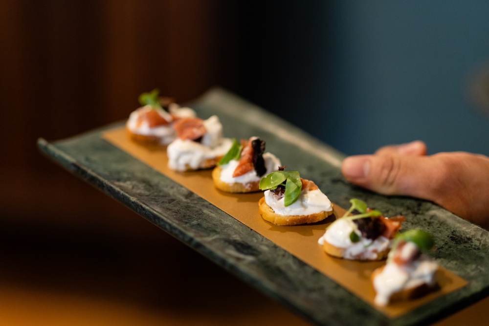 A close-up of a slate serving platter with colorful crustini appetizers. 