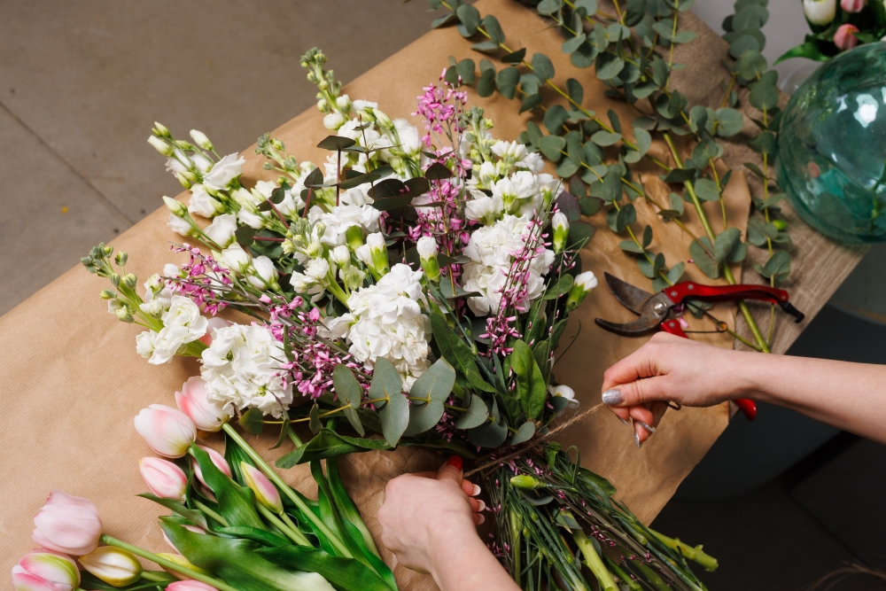 A woman's hands tie twine around a bouquet of white and pink flowers. 