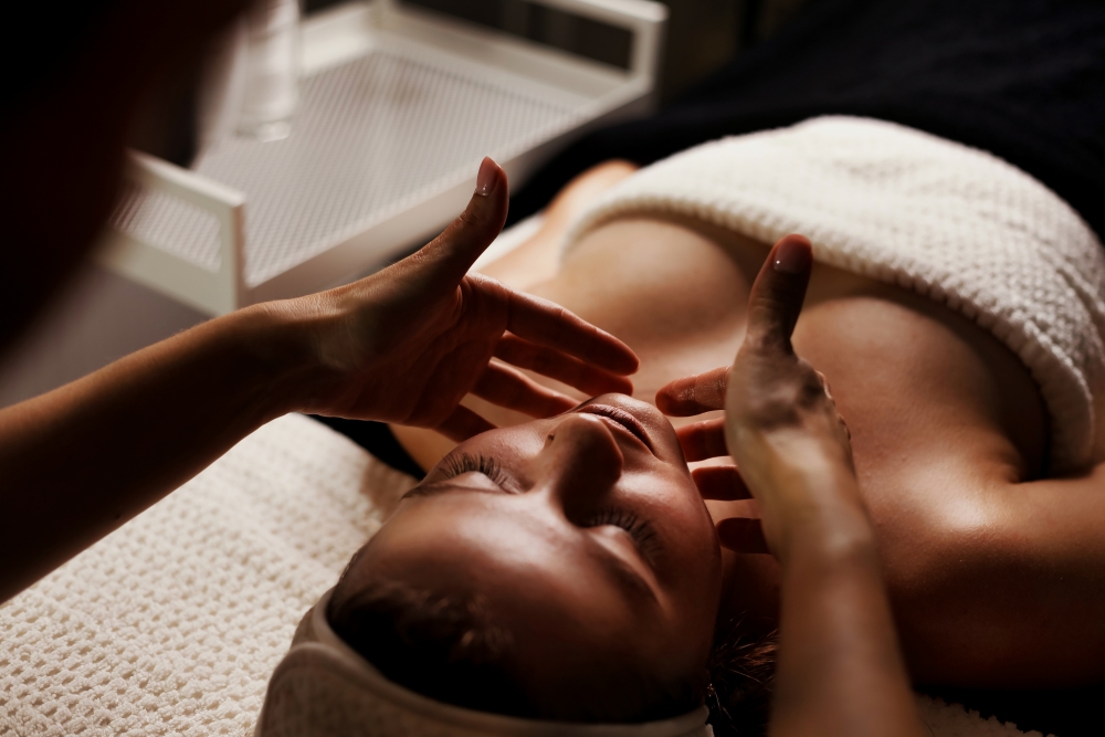 A woman lies on her back while a specialist gives her a facial. 