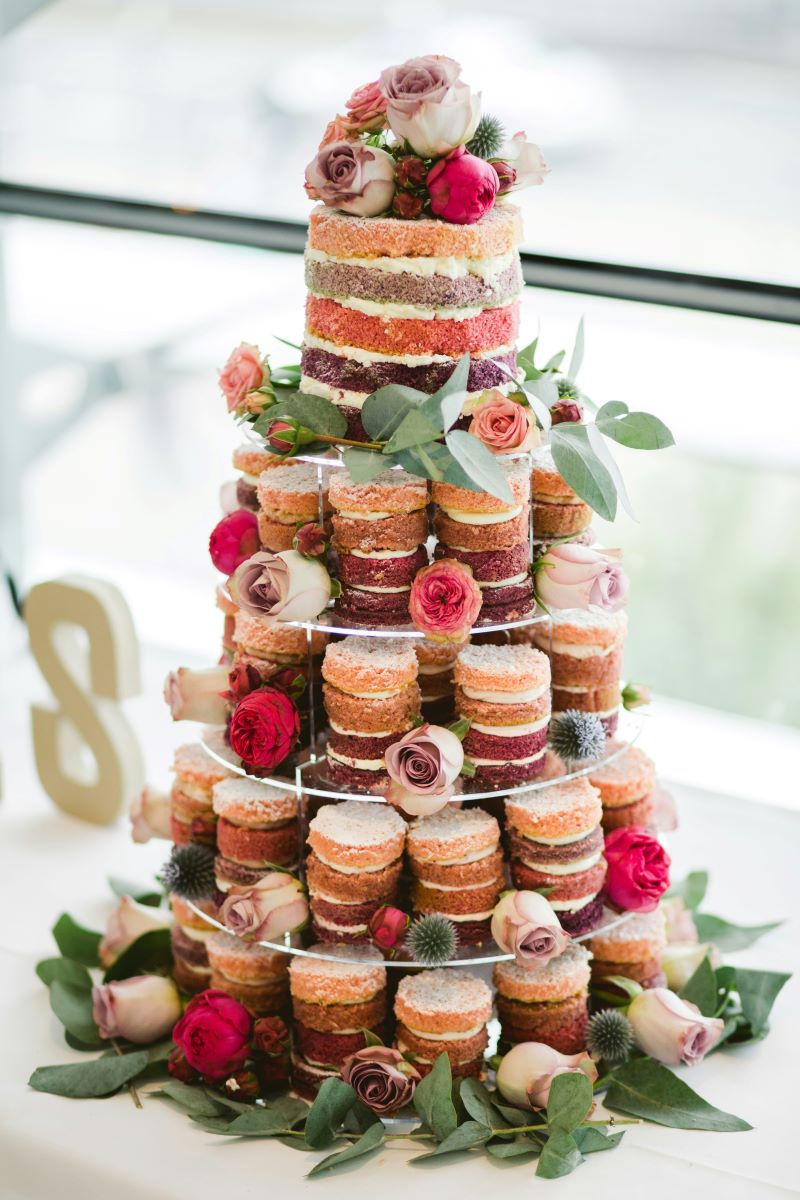 A colored tiered wedding cake made of stacks of small cakes, decorated with flowers and greenery. 