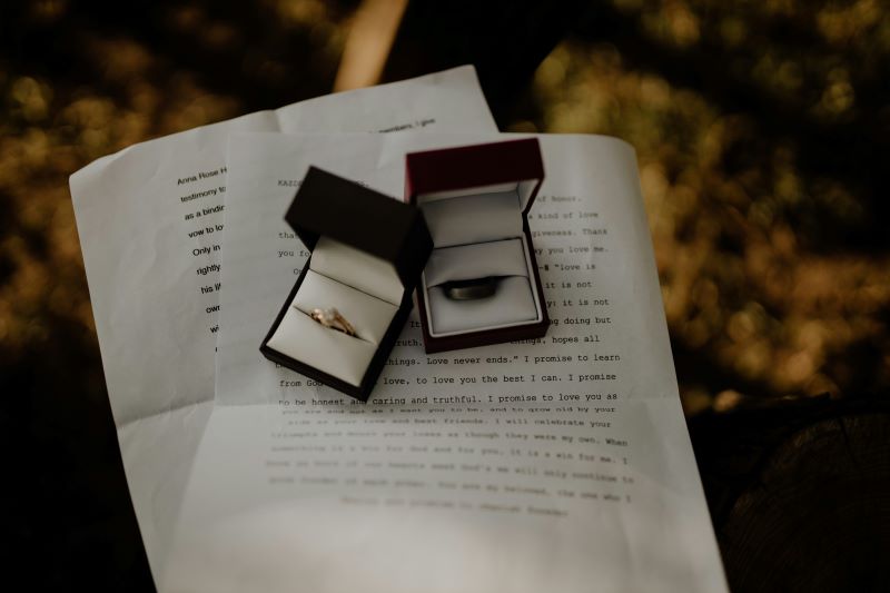 Two open ring boxes, one to the left with a gold diamond ring and the other one to the right with a plain band made of a dark metal, resting on top of a typed letter with wedding vows. Writing new vows is a special tip for renewing your wedding vows. 